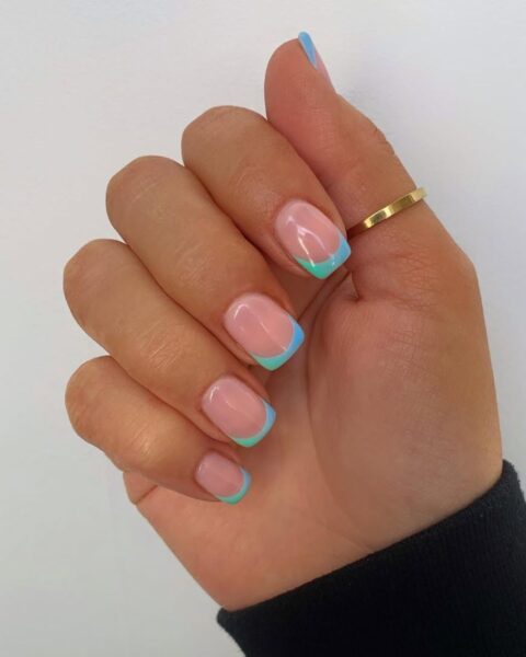 Zdjęcie dłoni z krótkimi, kwadratowymi paznokciami pomalowanymi w stylu french manicure ale z turkusową końcówką z dwoma odcieniami turkusu.