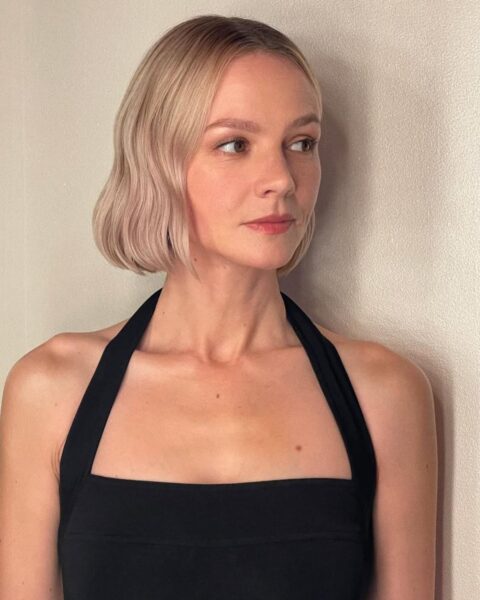 Zdjęcie aktorki Carey Mulligan w krótkich, blond włosach w stylu italian bob na lato 2025. Ubrana jest w czarny top halter. Pozuje na tle ściany, patrzy w bok.