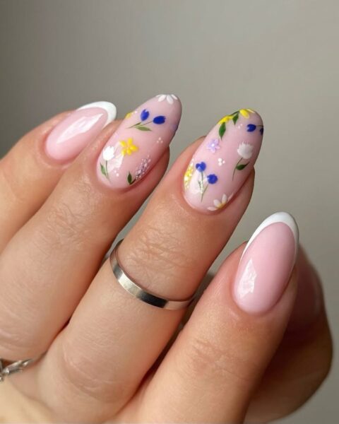 Zdjęcie dłoni ze zbliżeniem na długie, migdałowe paznokcie z french manicure i wzorem polnych kwiatów. Na palcach znajdują się srebrne pierścionki.