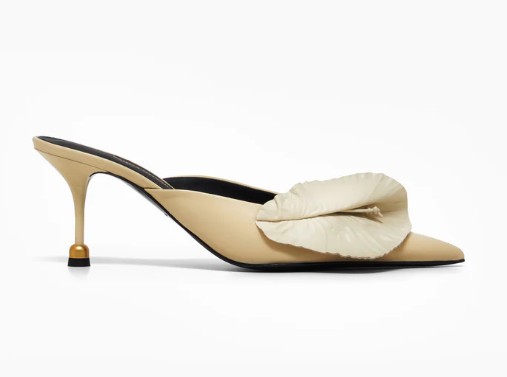 Beżowe buty z zakrytym przodem i odkrytą piętą. Buty na obcasie zakończonym złotym elementem. Na czubku beżowy kwiat.