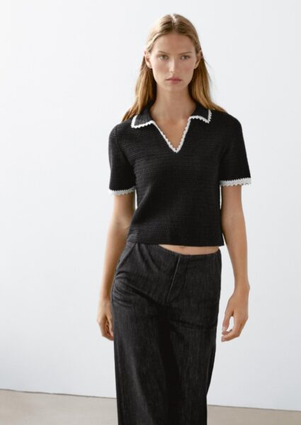 Modelka w ciemnym polo i ciemnej spódnicy.