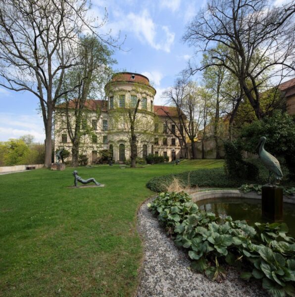 Stary budynek - pałac. Na pierwszym planie ogród i drzewa.