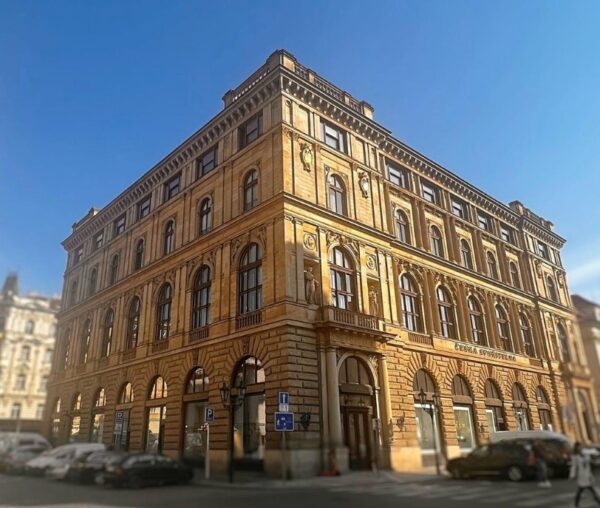 Stary, prosty budynek. Przed budynkiem ulica.