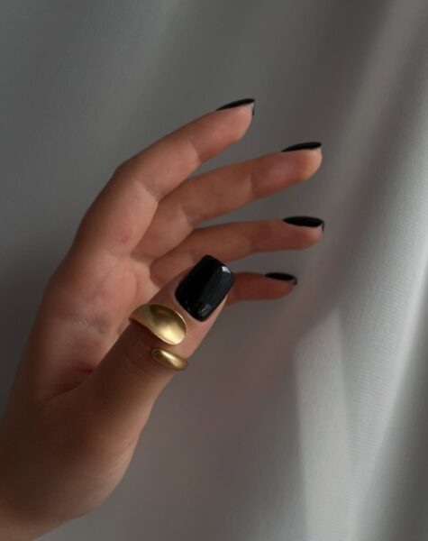 Kobieca dłoń z czarnymi manicure. Kobieta ma na kciuku złoty pierścionek.