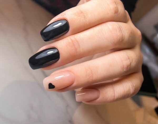 Manicure - dwa czarne paznokcie i dwa jasne. Na jasnym widniejsze małe, czarne serce.