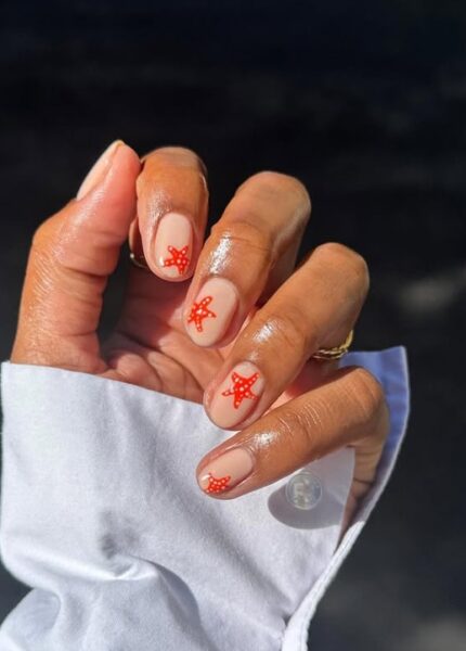 Jasny manicure z pomarańczową rozgwiazdą na płytce. Widać mankiet białej koszuli.