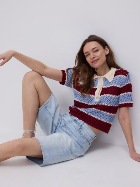 Modelka w jeansowych shortach i koszulce polo w niebiesko-brązowe pasy.