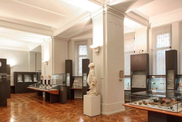 Beżowo-drewniane wnętrze muzeum. Sala wystawowa z gablotami rzeźbami.