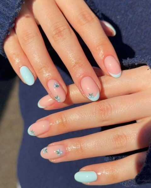 Zdjęcie dłoni ze zbliżeniem na długie, migdałowe paznokcie ozdobione french manicure w kolorze turkusowym i ozdobione wzorem borówek.