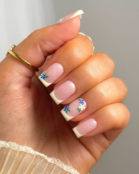 Zdjęcie dłoni z długimi, kwadratowymi paznokciami ze wzorem french manicure w kolorze żółtym i ze wzorem borówek.
