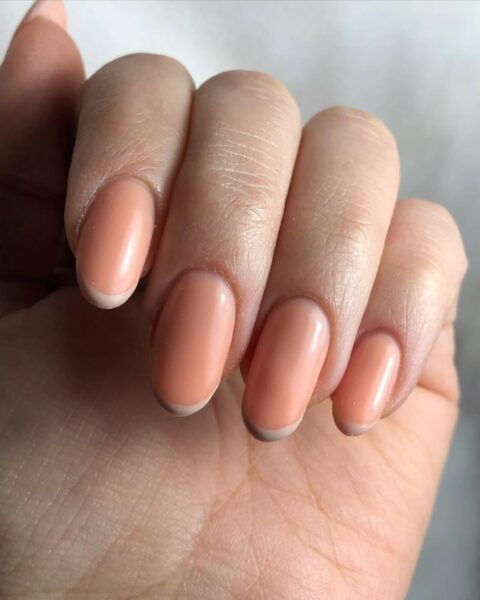 Zdjęcie dłoni ze zbliżeniem na długie, migdałowe paznokcie. Są pomalowane na kolor brzoskwiniowy i mają kremowe końcówki w stylu french manicure.