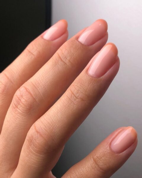 Zdjęcie dłoni z krótkimi, kwadratowymi paznokciami z zaokrąglonymi bokami. Są pomalowane na kolor nude i z brzoskwiniową końcówką w stylu french manicure.