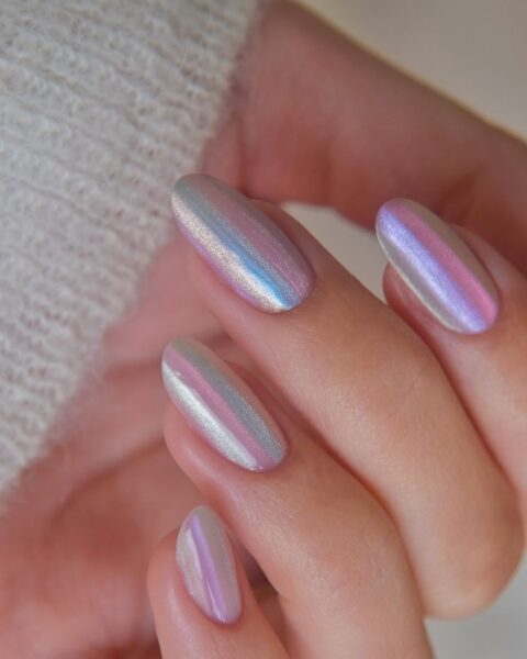 Zdjęcie dłoni z mocnym zbliżeniem na chromatyczny manicure: paznokcie są długie, migdałowe, ozdobione wzorem w paski z chromowanym wykończeniem.