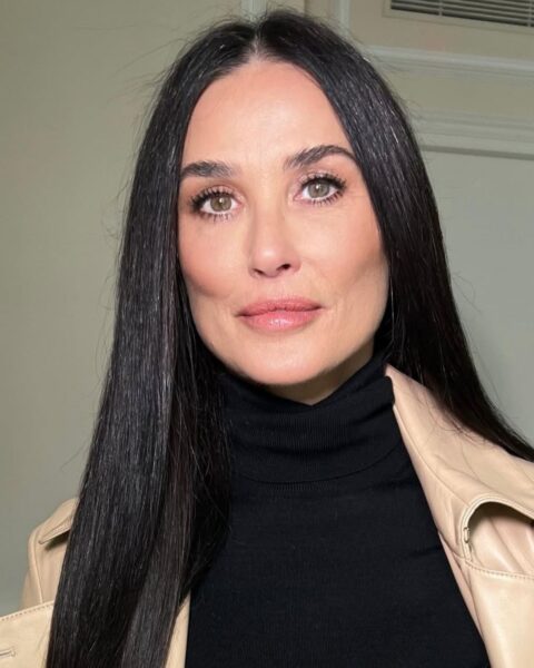 Zdjęcie aktorki Demi Moore. Ma długie, proste włosy, rozpuszczone. Ubrana jest w czarny sweter z golfem oraz beżową, skórzaną kurtkę. Ma lekki makijaż i modne, delikatnie pomalowane brwi.