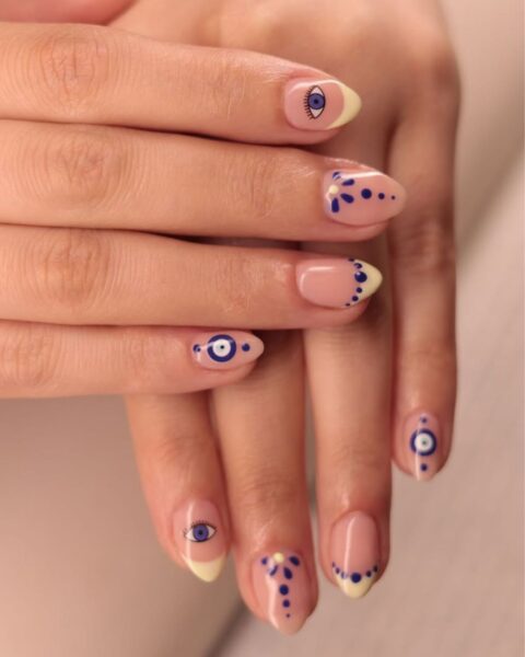 Zdjęcie dłoni z krótkimi, owalnymi paznokciami z żółtym french manicure oraz motywem oka proroka.