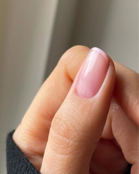 Zdjęcie dłoni ze zbliżeniem na kciuk pomalowany na styl french manicure z różową bazą i różową końcówką.