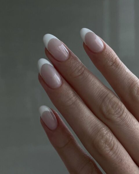 Zdjęcie dłoni ze zbliżeniem na paznokcie o owalnym kształcie pomalowane w stylu klasycznego french manicure.