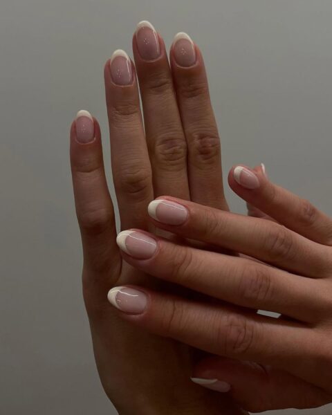 Zdjęcie dłoni ze zbliżeniem na paznokcie. Są średniej długości, owalne i pomalowane w stylu french manicure. Dłonie pozują tak, by prezentować manicure.