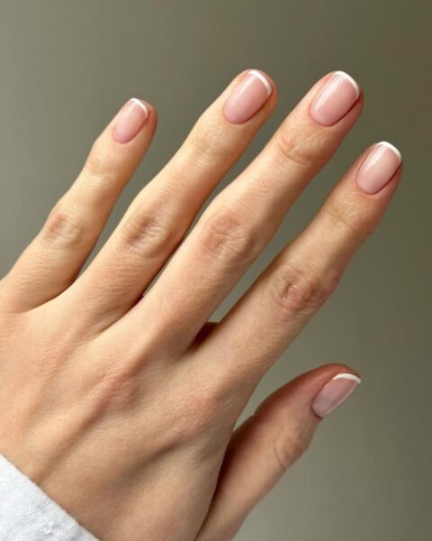 Zdjęcie dłoni z krótkimi paznokciami o kształcie zaokrąglonego kwadratu i pomalowane w stylu micro french manicure.
