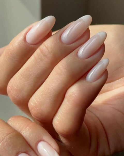 Zdjęcie dłoni z długimi, owalnymi paznokciami z french manicure w stylu soft z delikatnymi kolorami bieli, dzięki czemu ten french nie jest taki kontrastowy.