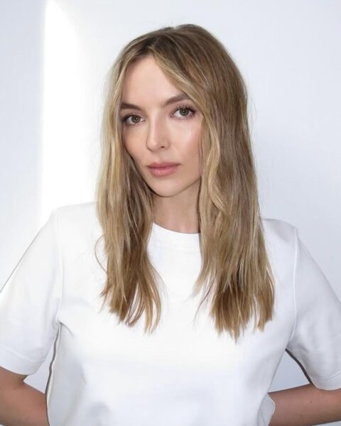 Zdjęcie kobiety w blond włosach do ramion i z długą, cieniowaną grzywką typu bottleneck. Kobieta ubrana jest w biały T-shirt. Pozuje na tle białej ściany.