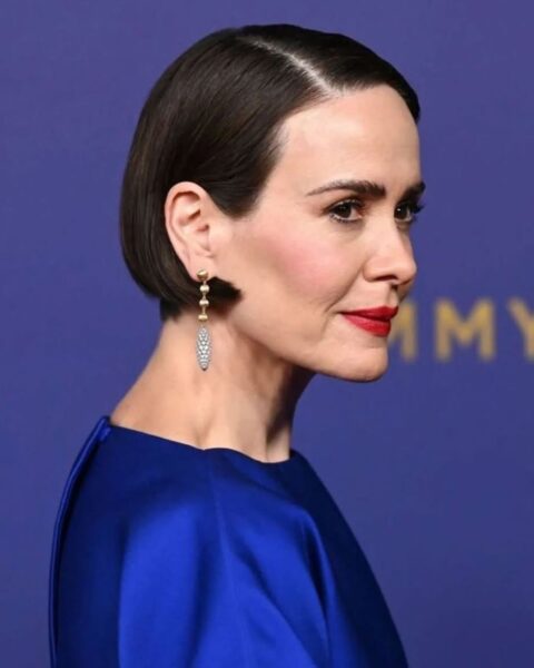 Zdjęcie aktorki, Sarah Paulson podczas jednej z galii. Jest ubrana w niebieską sukienkę i ma boba w stylu francuskim. Pozuje półbokiem. W uszach ma wiszące kolczyki.
