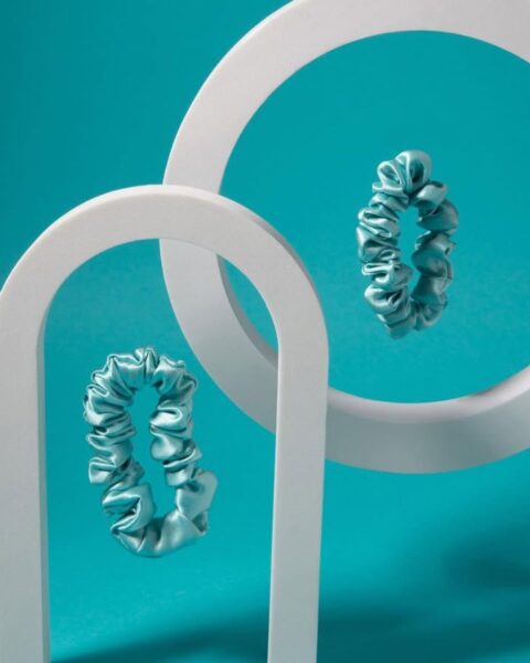 Zdjęcie produktowe przedstawiające gumki do włosów typu scrunchie w kolorze turkusowym. Są to zdjęcia produktowe, na niebieskim tle na białych stojakach.