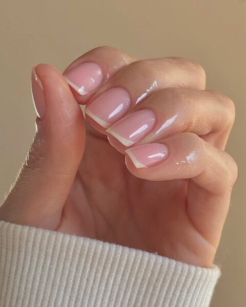 Zdjęcie dłoni ze zbliżeniem na średniej długości, kwadratowe paznokcie z french manicure. Palce są pokryte odżywiającą oliwką.