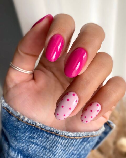 Zdjęcie dłoni z długimi, owalnymi paznokciami. Trzy paznokcie są pomalowane na kolor malinowy, a dwa na jasny róż i ozdobione wzorem polka dots w kolorze malinowym.