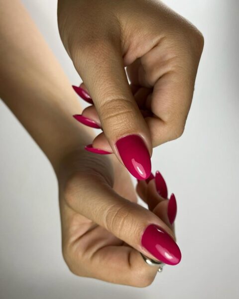 Zdjęcie dłoni ze zbliżeniem na malinowy manicure na drugą połowę lipca. Paznokcie są owalne i długie. Dłonie pozują tak, by prezentować manicure.