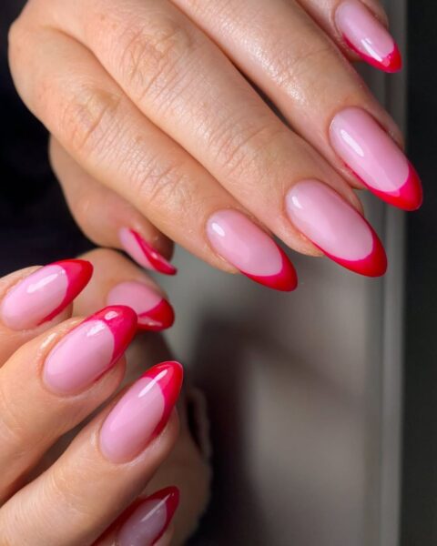 Zdjęcie dłoni z długimi, migdałowymi paznokciami w kolorze jasnego różu z kreską na brzegu w stylu french manicure, ale nie białą, a malinową.