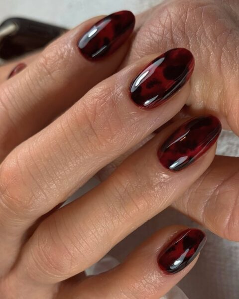 Zdjęcie dojrzałej dłoni z długimi, owalnymi paznokciami pomalowanymi na wzór szylkretowy. Dłonie układają się tak, by prezentować manicure.