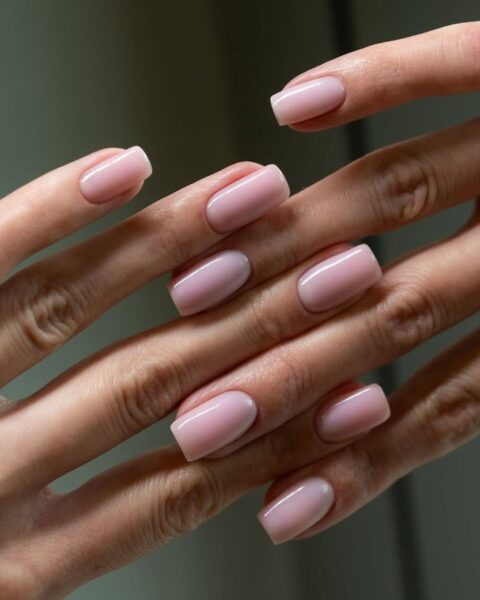 Zdjęcie dłoni z długimi, kwadratowymi paznokciami w kolorze jasnoróżowym w stylu luxorious pink. To manicure, który podkreśla opaleniznę. Dłonie pozują splecione i prezentują manicure.