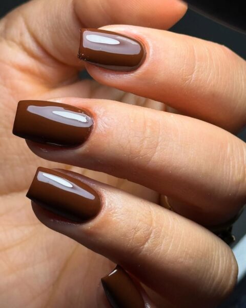 Zdjęcie dłoni ze zbliżeniem na manicure z długimi, kwadratowymi paznokciami w kolorze brązowym w stylu cannelle nails.