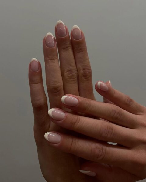 Zdjęcie dłoni ze zbliżeniem na średniej długości paznokcie o owalnym kształcie z klasycznym french manicure. Dłonie układają się tak, by prezentować manicure.
