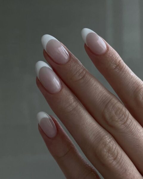 Zdjęcie dłoni ze owalnymi, średniej długości paznokciami pomalowanymi w stylu french manicure.