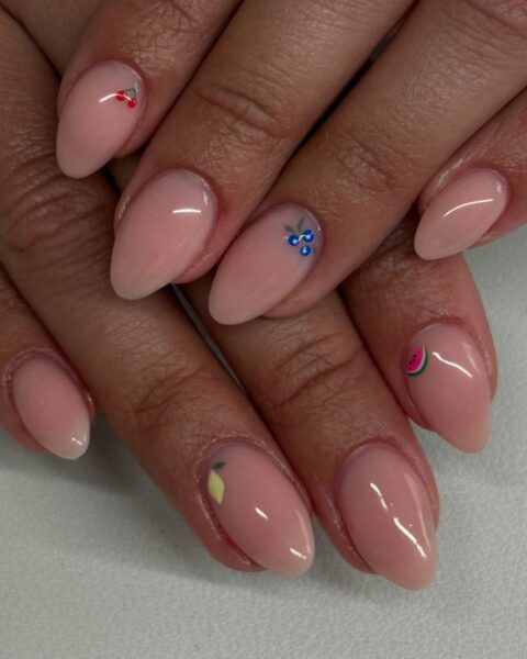 Zdjęcie dłoni ze zbliżeniem na długie, owalne paznokcie. Są pomalowane na kolor nude i ozdobione wzorem micro fruit manicure. Dłonie pozują jedna na drugiej, by prezentować manicure.
