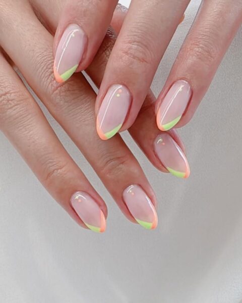 Zdjęcie dłoni z długimi, migdałowymi paznokciami w kolorze nude z kreskami na brzegu w stylu french manicure w kolorze pomarańczowo-limonkowym.
