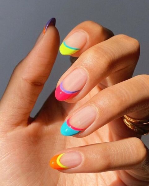 Zdjęcie dłoni z długimi paznokciami o owalnym kształcie, pomalowane w stylu double french manicure z neonowymi, kolorowymi paskami.
