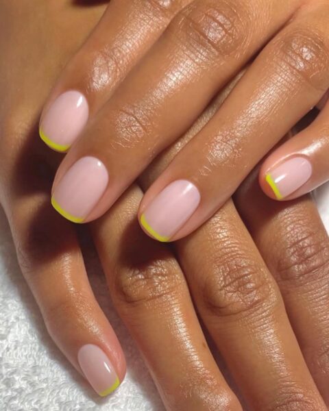 Zdjęcie dłoni ze zbliżeniem na krótkie, kwadratowe paznokcie z micro french manicure w neonowym kolorze limonki. Dłonie pozują tak, by prezentować manicure, oparte jedna o drugą na białym ręczniku.