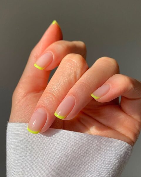 Zdjęcie dłoni z krótkimi, kwadratowymi paznokciami, które zdobi neonowy french manicure na lipiec, czyli z limonkowymi końcówkami.