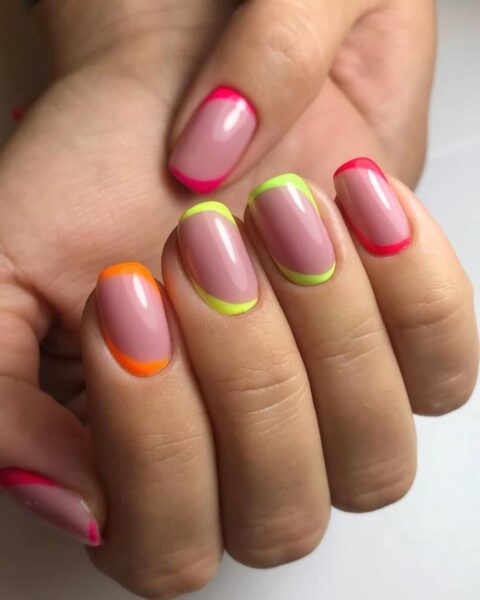 Zdjęcie dłoni z długimi, kwadratowymi paznokciami ozdobione neonowymi kreskami na brzegu paznokci i u nasady paznokci. Dłonie pozują tak, by prezentować manicure na białym blacie stołu.