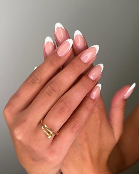 Zdjęcie dłoni ze zbliżeniem na długie, owalne paznokcie pomalowane na wzór french manicure. Na palcu serdecznym jednej z dłoni widać złoty pierścionek Cartier z gwoździem. Dłonie układają się tak, by prezentować manicure.
