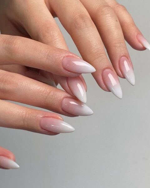 Zdjęcie dłoni ze zbliżeniem na długie, migdałowe paznokcie. Są ozdobione wzorem baby boomer. Dłonie pozują tak, by prezentować manicure.
