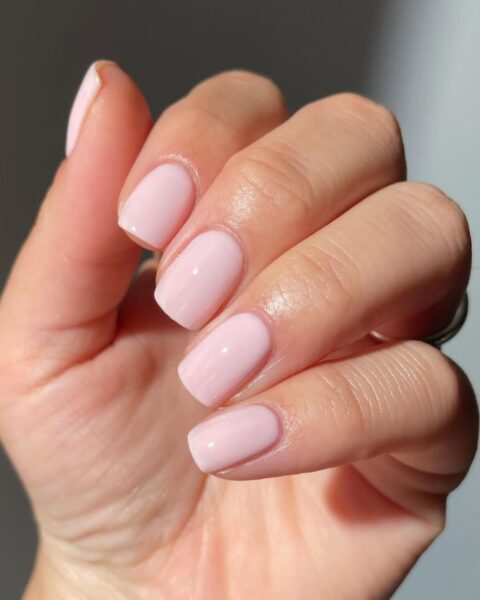 Zdjęcie dłoni ze zbliżeniem na krótkie, kwadratowe paznokcie pomalowane na kolor nude w stylu princess nails.