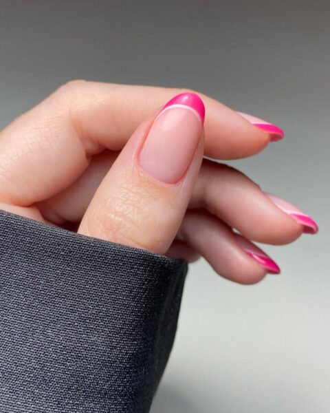 Zdjęcie dłoni z długimi, owalnymi paznokciami. Są pomalowane na wzór double french manicure, gdzie przy brzegu paznokcia znajduje się różowa oraz biała kreska.
