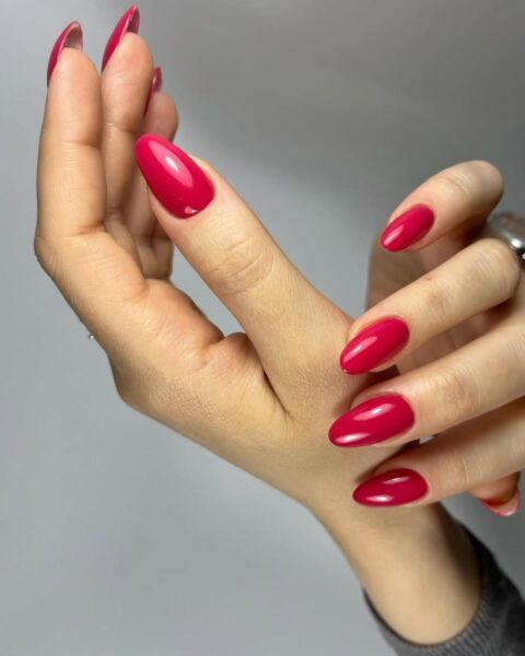 Zdjęcie dłoni ze zbliżeniem na poziomkowy manicure: długie, migdałowe paznokcie w kolorze poziomkowego różu. Dłonie układają się tak, by prezentować manicure.