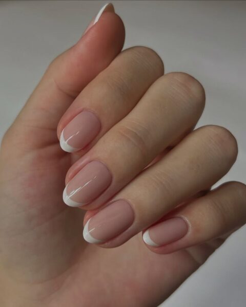 Zdjęcie dłoni ze zbliżeniem na długie, owalne paznokcie. Są pomalowane na wzór klasycznego french manicure.
