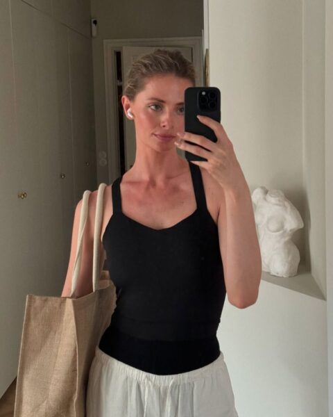Zdjęcie kobiety, która zrobiła sobie selfie w lustrze. Ma blond włosy związane w kucyk. Ubrana jest w czarny top na ramiączkach i beżowe, sportowe spodnie z wiązaniem w pasie. Na ramieniu ma płócienną torbę. Wybiera się na ćwiczenia.