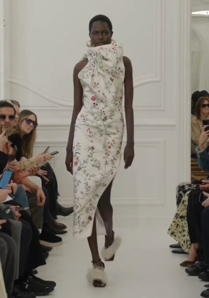 Modelka na wybiegu w jasnej, midi sukience w kwiaty.